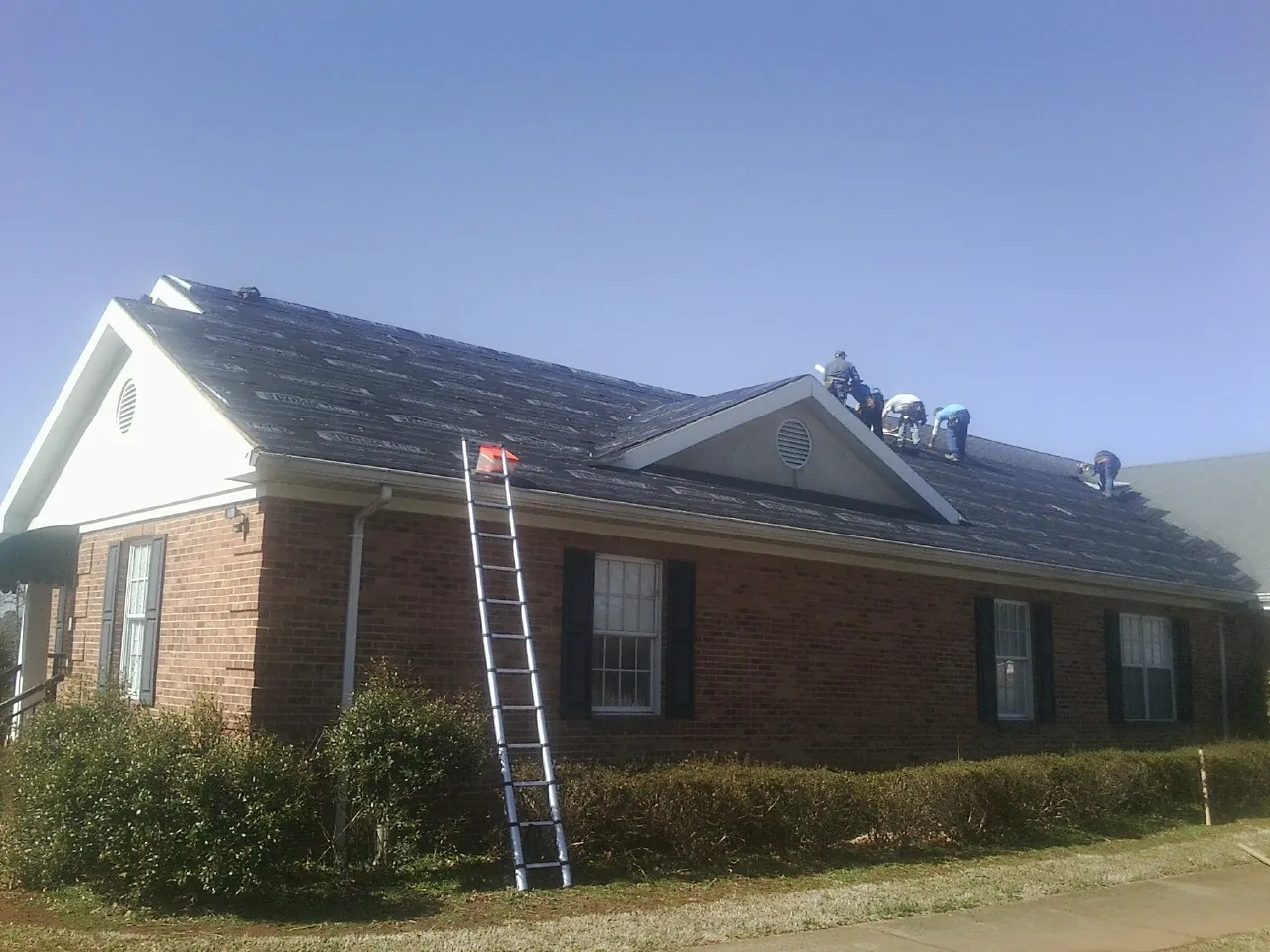 Crew tearing shingles off a brick ranch roof with a ladder set — Metal Roof Repair work by our crew in Ventura