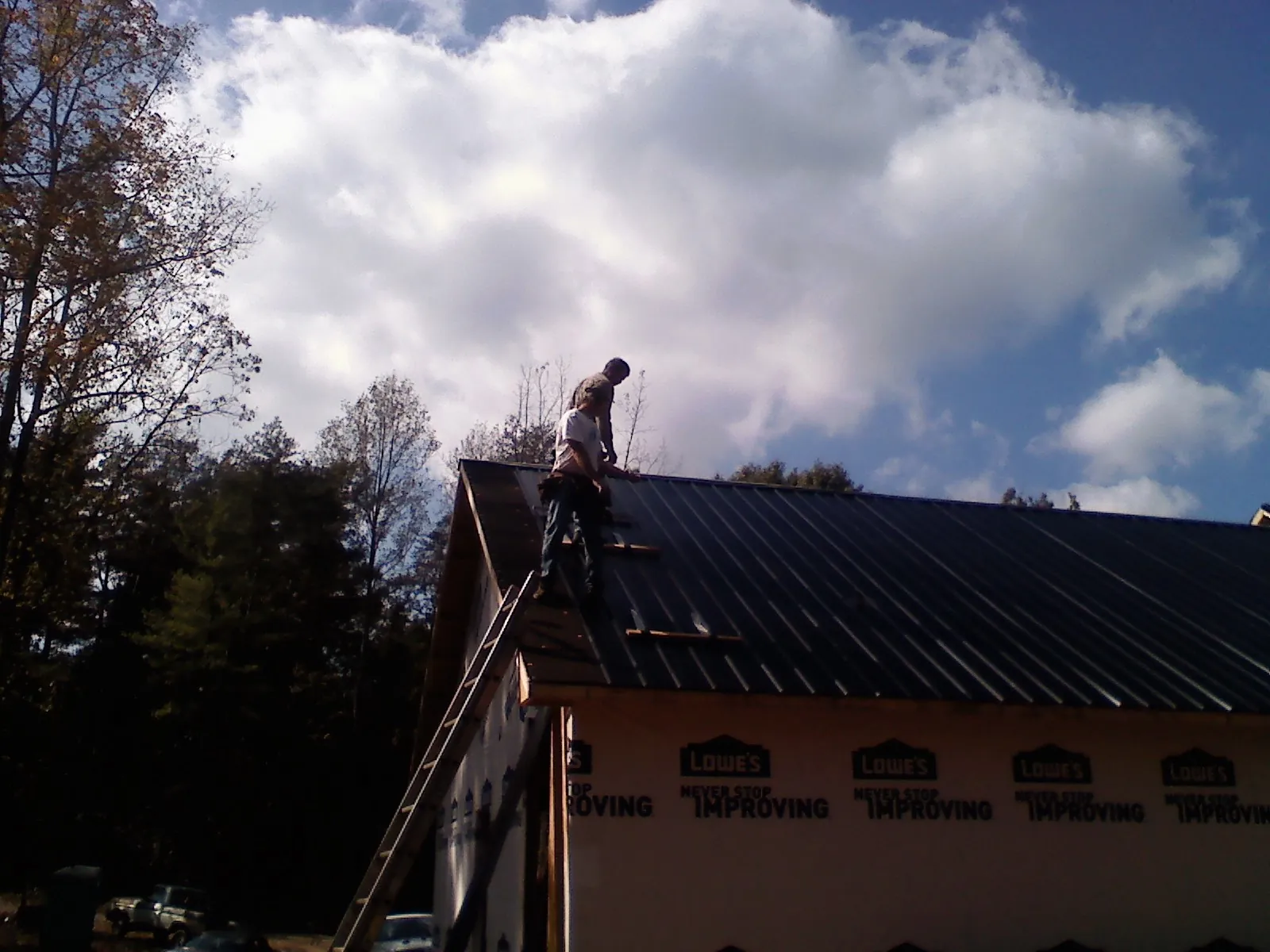 Roofer fastening dark metal panels high against a cloudy sky, from a Roof Inspection job in Ventura