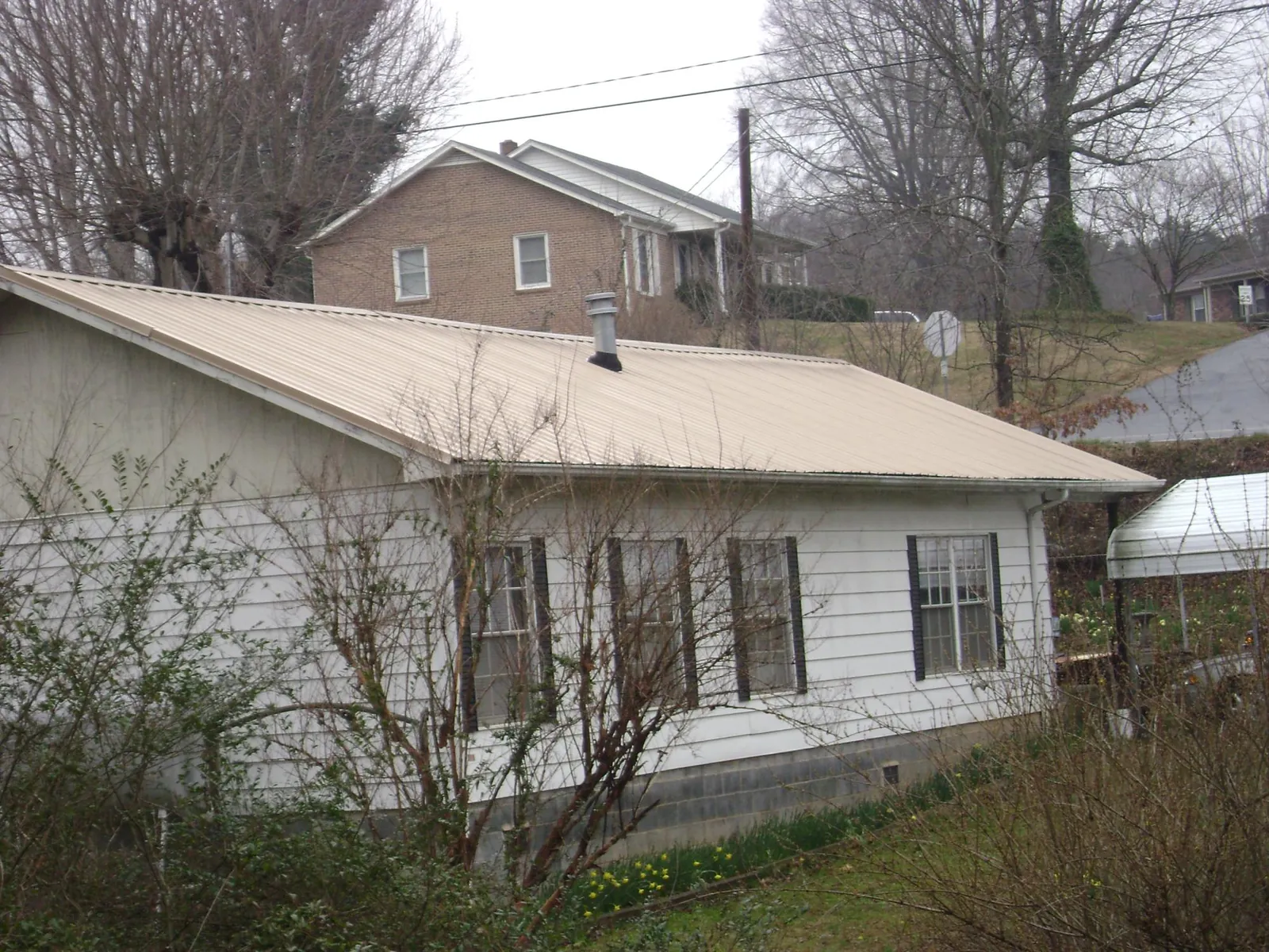Tan metal roof on a white sided house set into a hillside — Commercial Roofing by Roofing Brothers in Ventura